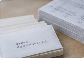 机に積まれた白い封筒の束と宛名リスト
